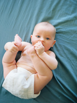 Baby lying on bed holding feet