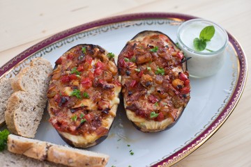 Stuffed Eggplant halves with tomato onion sweet pepper and cheese baked and served with small pieces of whole grain bread roll and greek style sauce made from yogurt, cucumber, garlic and mint leaves