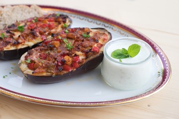 Stuffed Eggplant halves with tomato onion sweet pepper and cheese baked and served with small pieces of whole grain bread roll and greek style sauce made from yogurt, cucumber, garlic and mint leaves