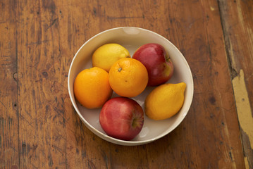 oranges, apples and lemons on rustic plate on wooden table  