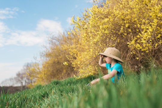 Young boy sitting in field, wearing safari hat, looking at view