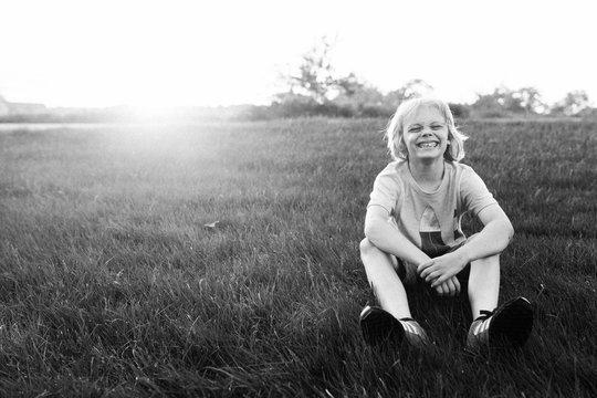 Young boy sitting on grass, smiling, black and white