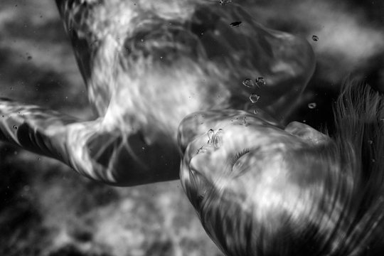 Young boy floating underwater, close-up, black and white
