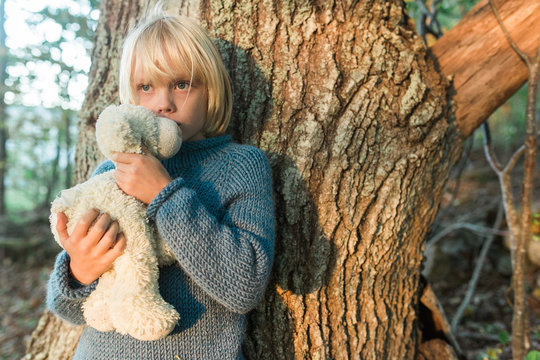 Young boy leaning against tree, holding soft toy