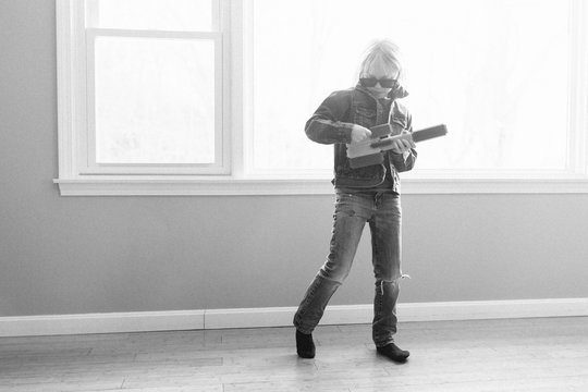 Young boy playing pretend guitar in empty room, black and white