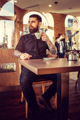 A man with tattooes on his arms in a cafe.