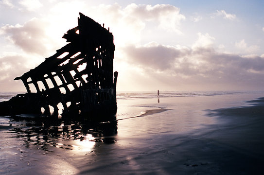 Sunset over a shipwreck on a beach with a tiny figure in the distance