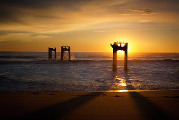 Silhouette of dilapidated pier supports in ocean at sunset