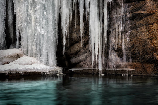 Icicles on rockface by frozen lake 