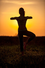 Silhouette of young woman meditating against sunset background