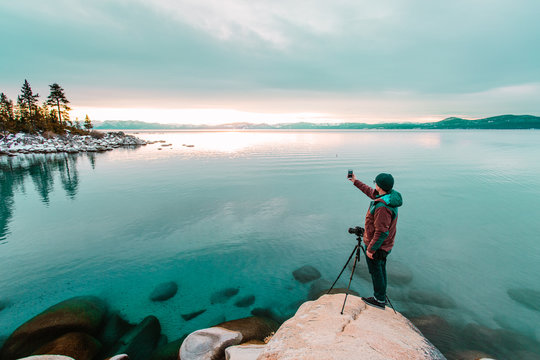 Man by lake Tahoe using smartphone to take photograph