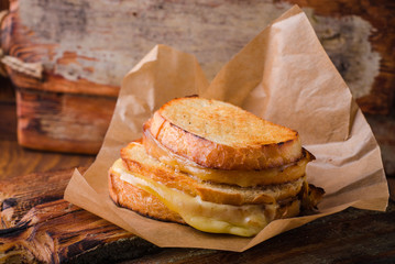 Grilled cheese sandwich on paper on wooden board. Selective focus.