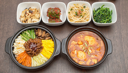 Korean bibimbap and kimchi soup with side dishes on wooden table