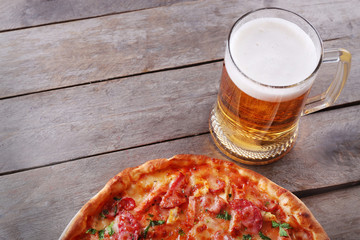 Tasty pizza and glass of beer are on wooden table, close up
