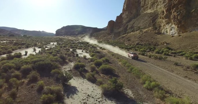 Aerial scene of car traveling on dirt road a dry, rocky, landscape. Monumental scenery. Car leves dust while driving. Fast scene. Canyon of Piedra Parada, Chubut, Patagonia Argentina. Hiking place. 