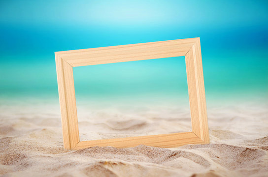 Empty wooden picture frame on the beach sand, summer concept.
