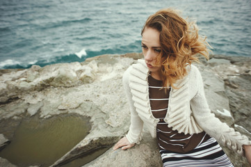 sexy blonde wearing dress with stripes and cardigan posing on rock in the sea