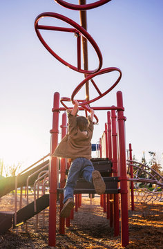 Rear view of boy swinging on monkey bars in playground