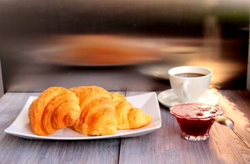 Breakfast - croissant, jam and coffee - served on a wooden table. Steel background with reflections.
