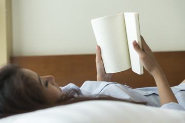 Fototapeta na wymiar Young woman reading book while lying on the bed