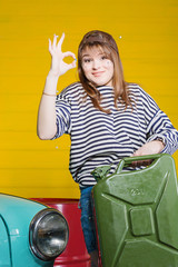 brunette woman in a cap and a striped sweater holding empty or full canister of gasoline in the garage near the retro car.