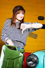 brunette woman in a cap and a striped sweater holding empty or full canister of gasoline in the garage near the retro car.