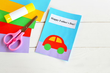 Paper card with red car and text Happy father's day. Colored paper, scissors, glue stick. Materials used in manufacture of handmade card. Paper handcraft greeting card for dad. Children creative craft