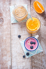 Fototapeta na wymiar A mix of three smoothies with blueberry, orange and peach on a wooden background with copy space, top view