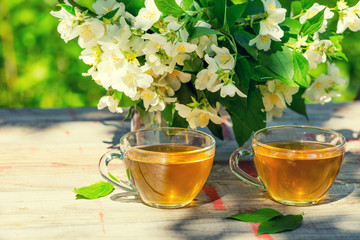 Two cups of green tea with jasmine flowers on grunge wooden table outdoors