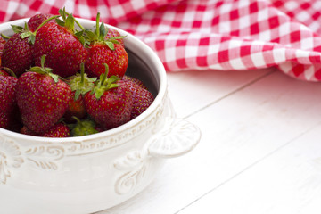 Fresh strawberries in bowl on a white wooden background