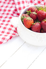 Fresh strawberries in bowl on a white wooden background