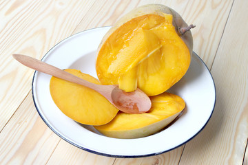 Delicious ripe mango fruit with wood spoon in whiter dish on wood background.