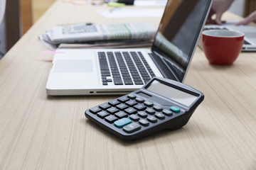 calculator, laptop computer, newspaper, coffee cup on wooden tab