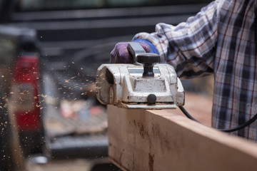 worker planing a wood with a electric plane