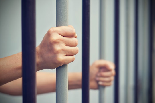 prisoner was locked in jail, hands hold captive iron bars 