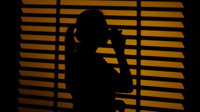 Woman drinking coffee from a cup. Silhouette. Close up