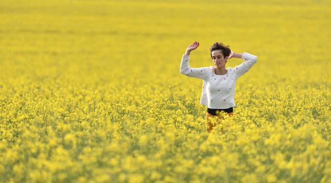 Young woman cheering in canola field in the summer