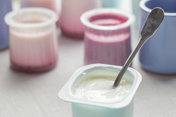 Yogurts assortment  in plastic bowls on light cloth background. Natural and fruit healthy, diet, gourmet dessert for granola breakfast. Sweet yoghurts closeup.