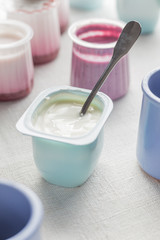 Yogurts assortment  in plastic bowls on light cloth background. Natural and fruit healthy, diet, gourmet dessert for granola breakfast. Sweet yoghurts closeup.