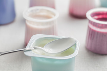 Yogurts assortment  in plastic bowls on light cloth background. Natural and fruit healthy, diet, gourmet dessert for granola breakfast. Sweet yoghurts closeup.