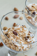 Granola with yoghurt, nuts and fruits in glass bowl on light background. Delicious, healthy sweet dessert for breakfast. Cereal, muesli.  Copy space, closeup.