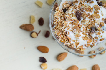 Granola with yoghurt, nuts and fruits in glass bowl on light background. Delicious, healthy sweet dessert for breakfast. Cereal, muesli.  Copy space, closeup.