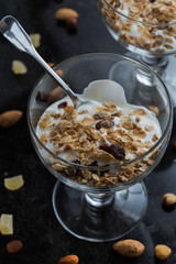 Granola with yoghurt, nuts and fruits in glass bowl on dark background. Delicious, healthy sweet dessert for breakfast. Cereal, muesli.  Copy space, closeup.