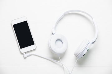 White headphones and smart phone on white wooden table