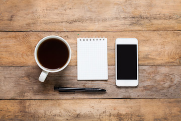 Top view White smart phone, note, pen, headphone and cup of coffee or tea on wooden background