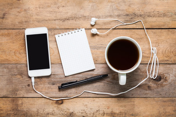 Top view White smart phone, note, pen, headphone and cup of coffee or tea on wooden background