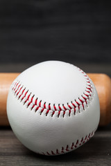 Baseball equipment: wooden bat and ball on a wood plank or bench background