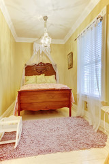 Carved wood bed with pillows in small yellow bedroom.