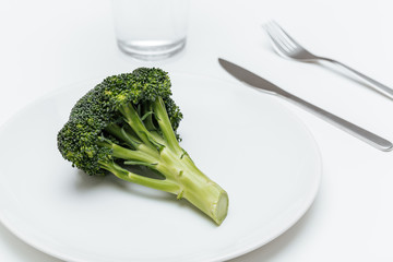 Glass of water, fork, knife and broccoli on the plate