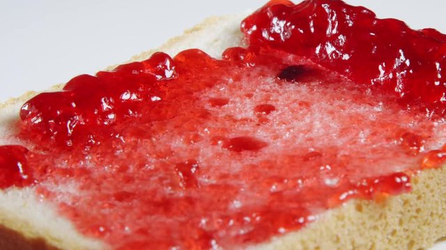 Human hand smears a cherry jam on a bread slice by a knife